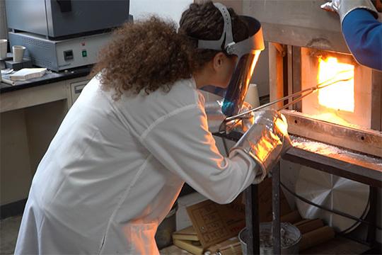 woman in lab coat removing material from furnace